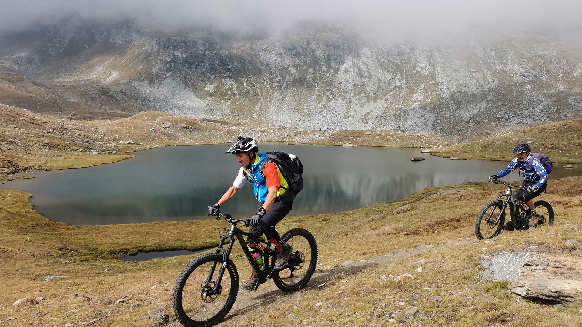 Due biker in mountain bike lungo un lago d'alta quota nel Parco Nazionale del Gran Paradiso Due biker in mountain bike lungo un lago d'alta quota nel Parco Nazionale del Gran Paradiso